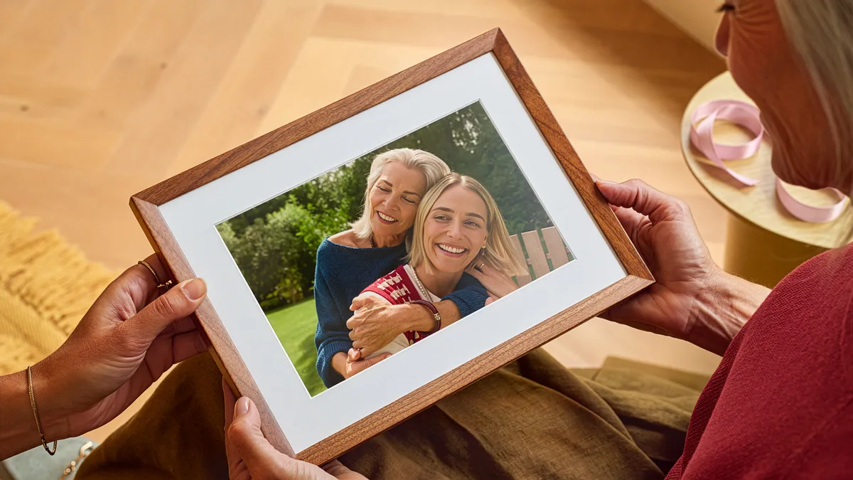 Hands holding the walnut Alexa Photo Frame showing a photo of two smiling women
