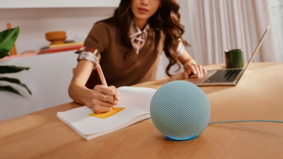 New Echo Dot in Agave Green on a desk next to a woman writing in a notebook