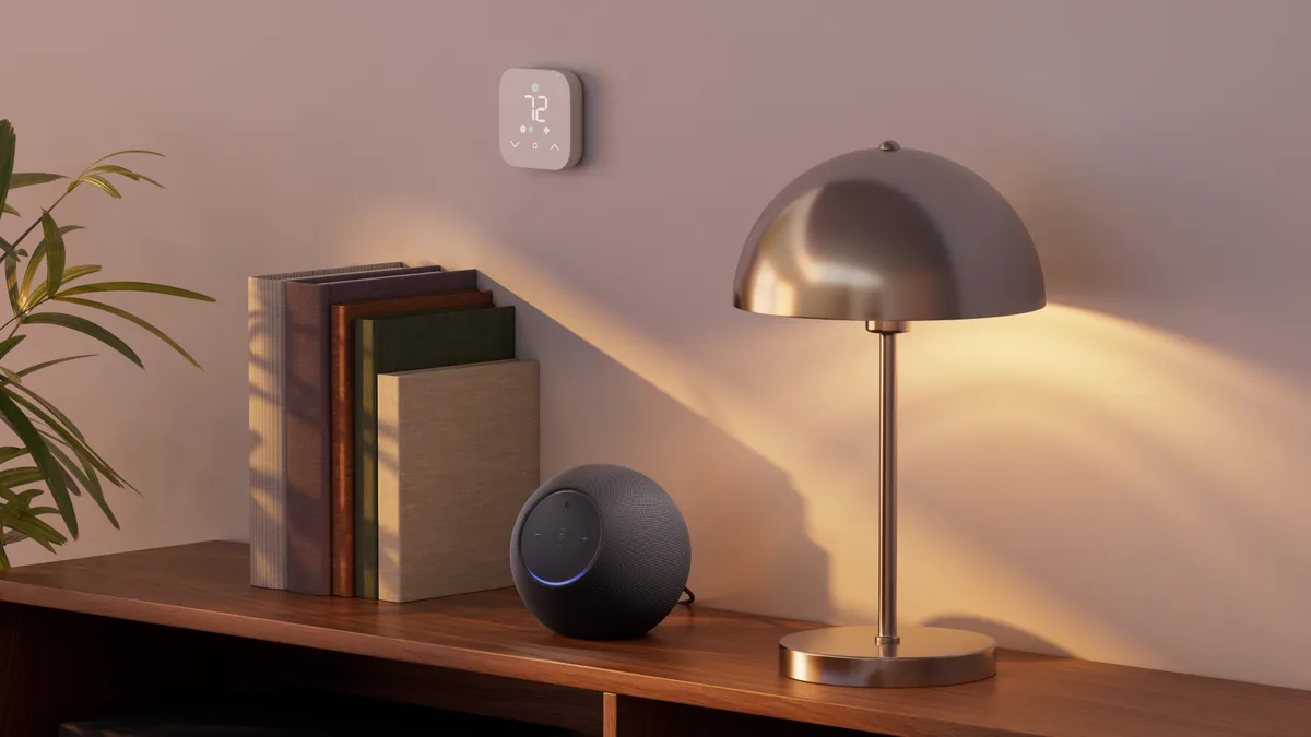 Echo Studio with Home Camera in Graphite on a wooden shelf beside books and a lamp